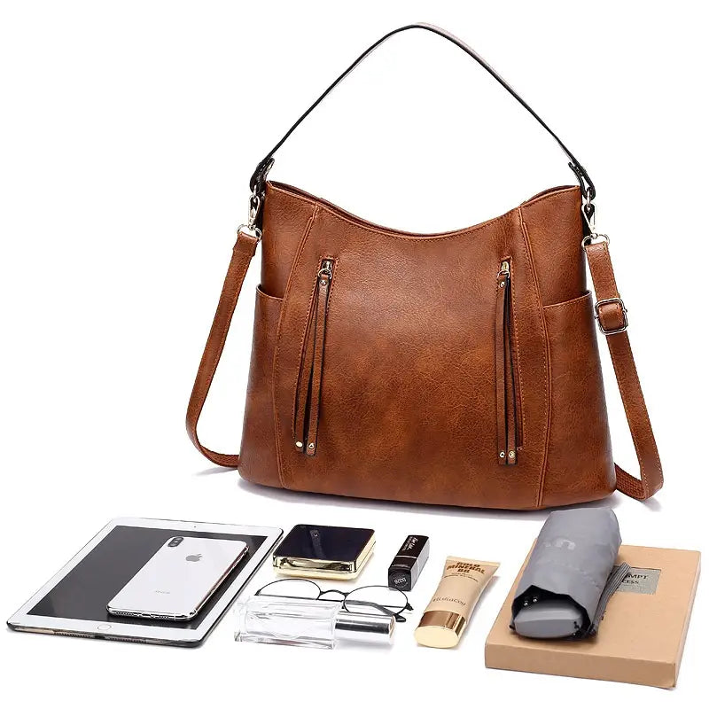 Brown faux leather hobo-style handbag with black shoulder straps, gold-tone zippers, tassel, and front zipper pockets.