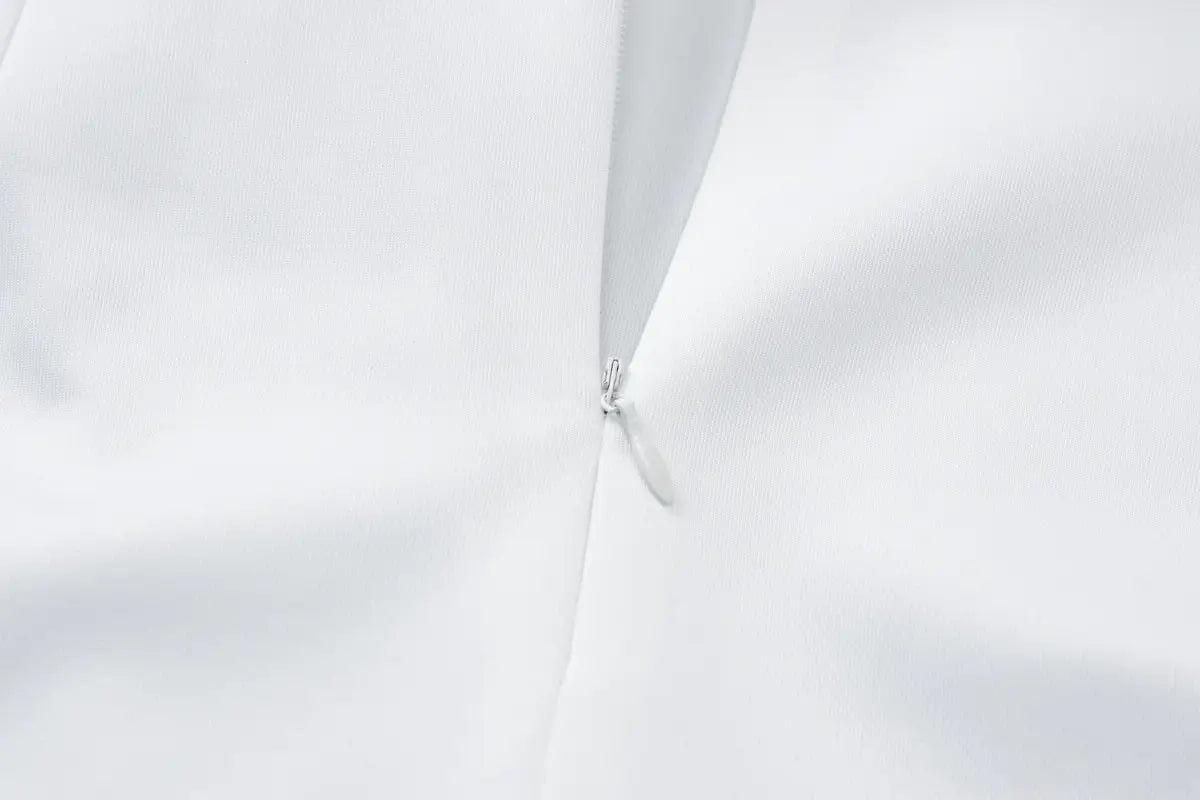A sleek silver zipper with a minimalist design on the back of a sequined off-the-shoulder white bodycon mini dress made of smooth fabric.