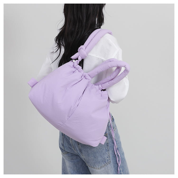A soft lavender quilted puffer tote bag made of lightweight nylon with padded knotted handles and a drawstring closure.