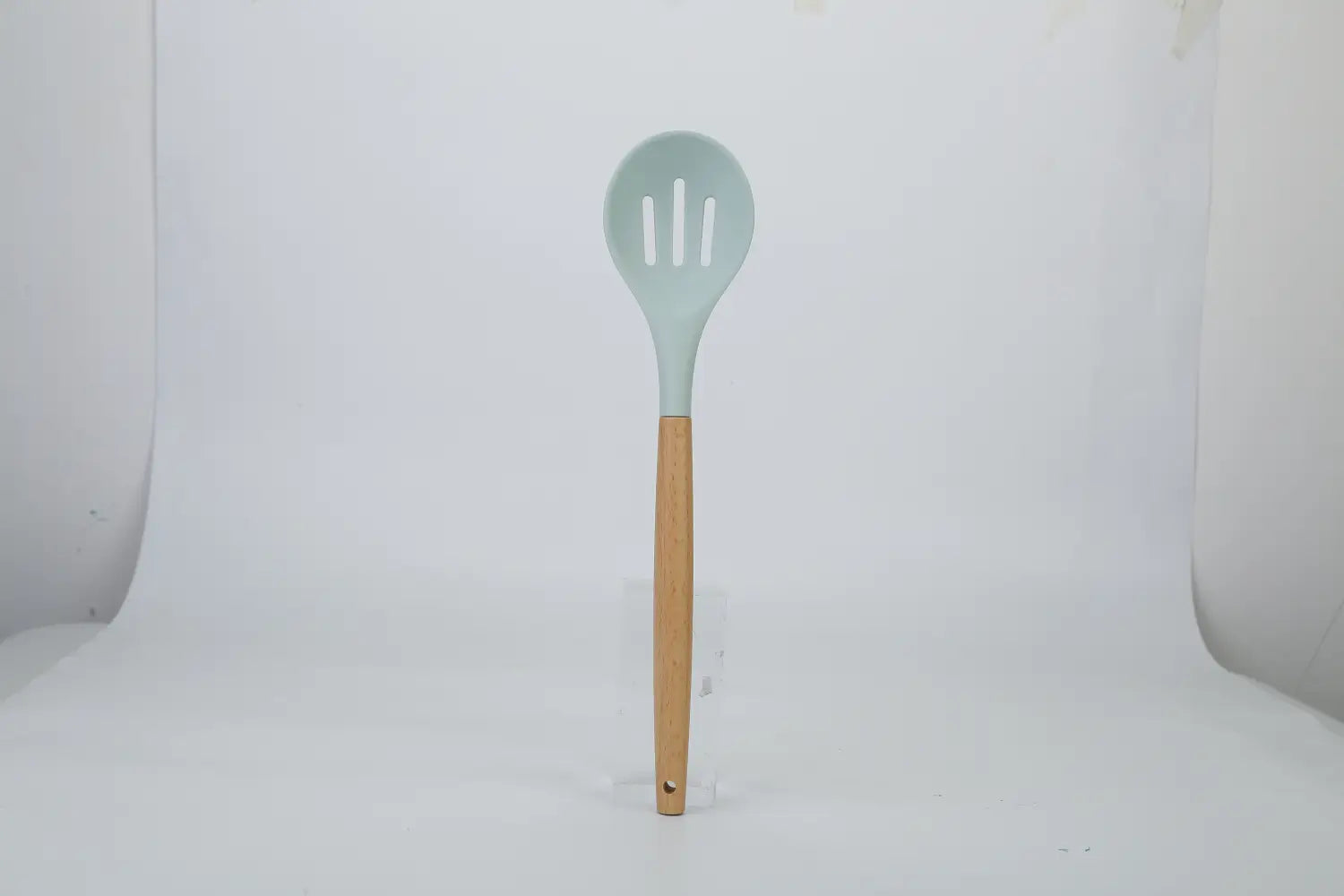 A light blue silicone slotted spoon with a wooden handle from the silicone cooking utensil set 11pc with wood handles.