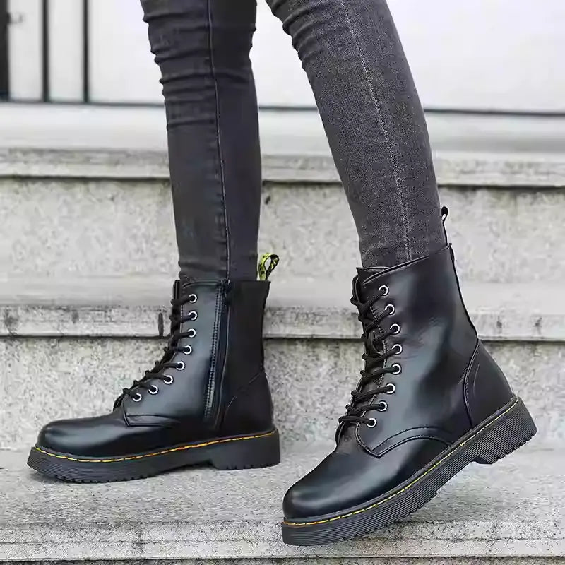 Botines estilo Martin de cuero negro con punta redonda, diseño con cordones, altura plana a la altura del tobillo, suela de goma gruesa y costuras amarillas.