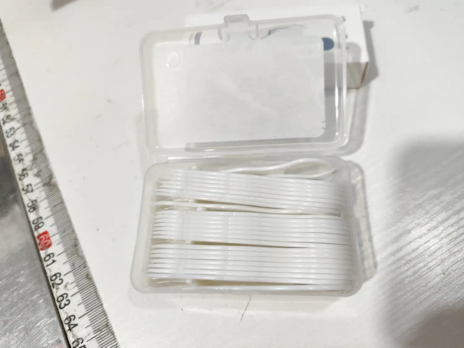 petits cure-dents pour fil dentaire en plastique blanc disposés de manière ordonnée dans une boîte de rangement transparente pour fil dentaire avec ouverture automatique à charnière
