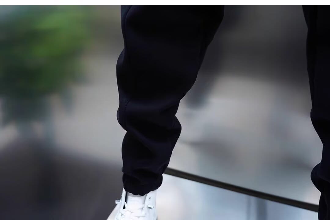 Mens casual solid color sweatpants in black featuring tapered legs and ribbed cuffs paired with white sneakers.
