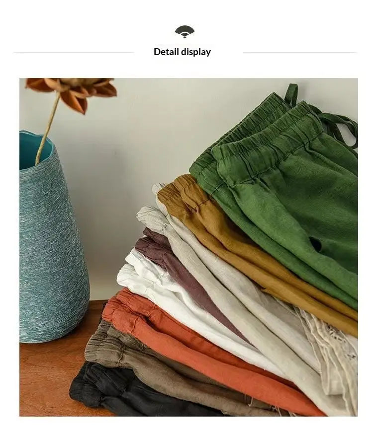 ein Stapel farbenfroher Baumwoll-Leinen-Hosen mit elastischem Bund und geradem Schnitt in erdigen Tönen, darunter Grün, Senf, Weiß und Schwarz.