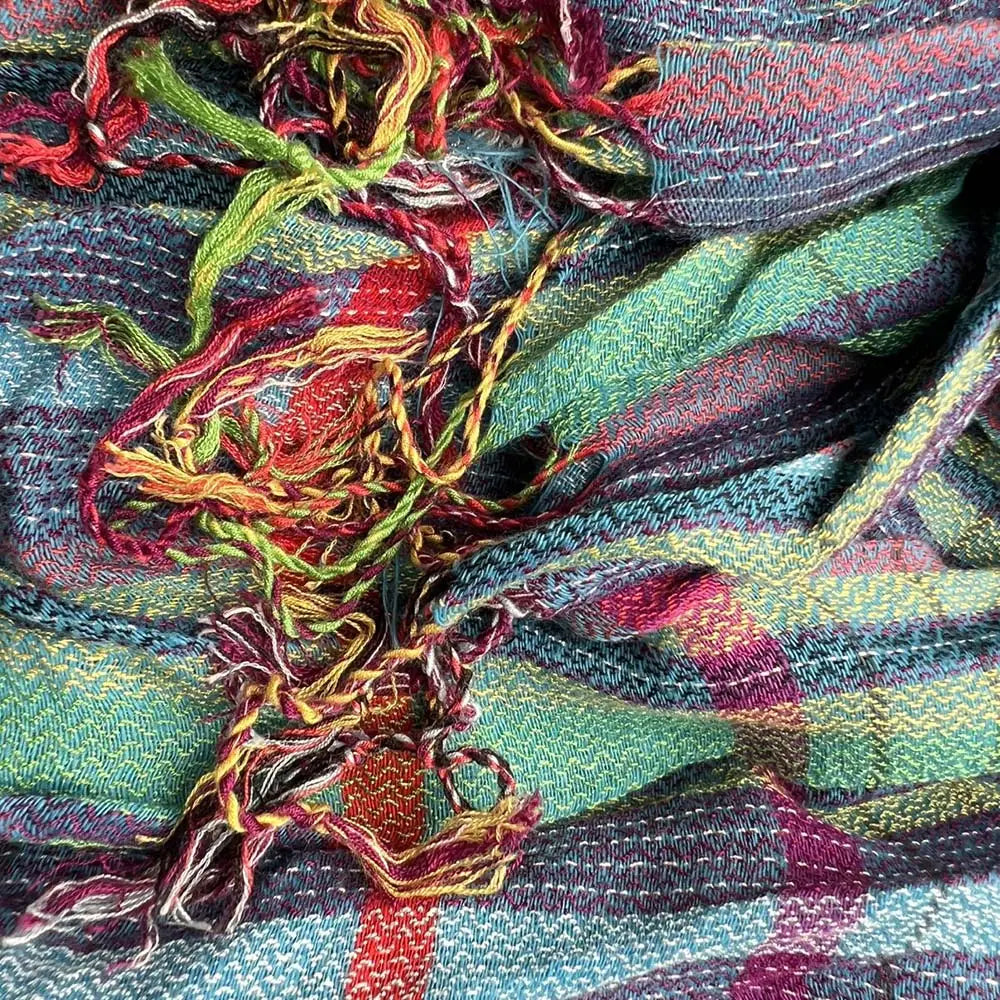 Une écharpe d’hiver bleue à jacquard texturé, dotée d’un motif écossais tissé coloré dans des nuances de vert, rouge, jaune, bleu et violet, avec des bords effilochés.