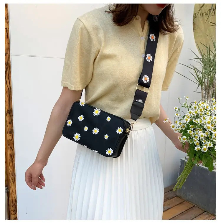 Black crossbody bag made of pu leather featuring white daisy embroidery and a matching chain strap for fashionable daily use.