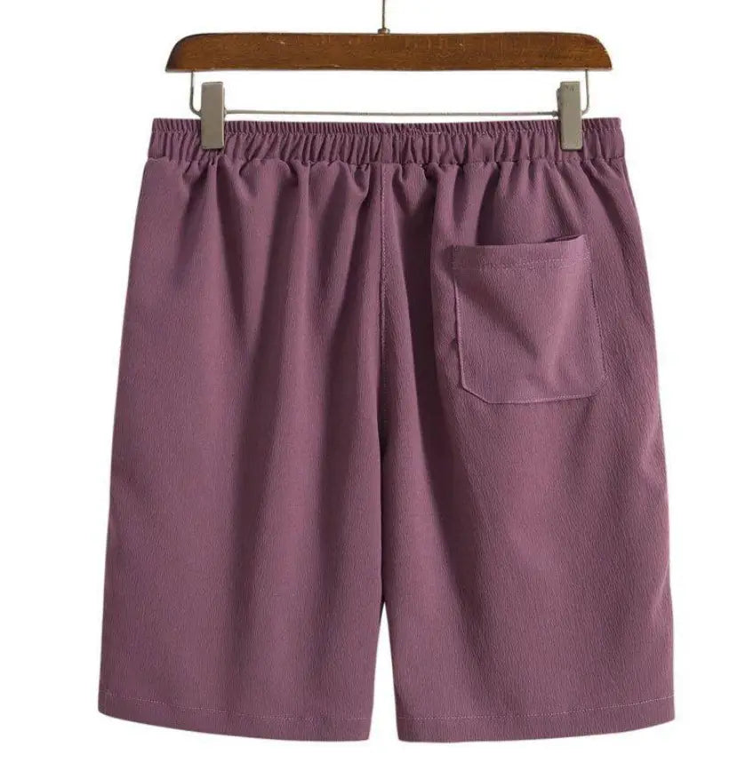 Short de plage en coton lin pour hommes de couleur violette, avec une ceinture élastique et une poche arrière unique, présenté depuis le côté arrière.