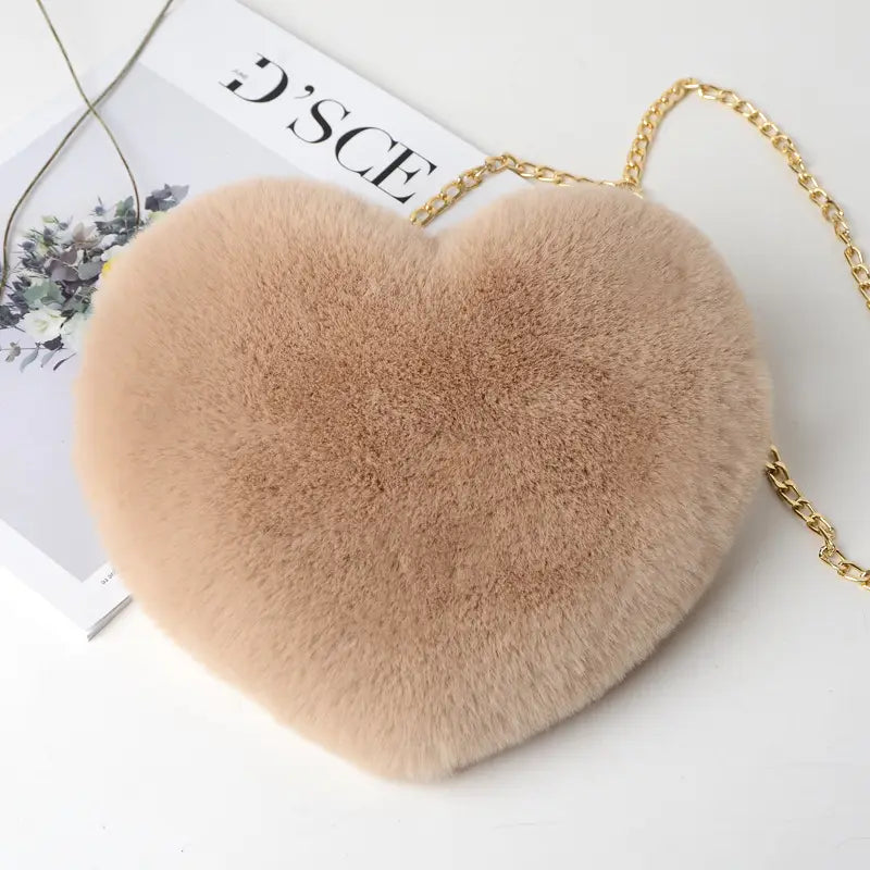 A soft beige plush faux fur heart shaped crossbody bag with a gold chain strap.
