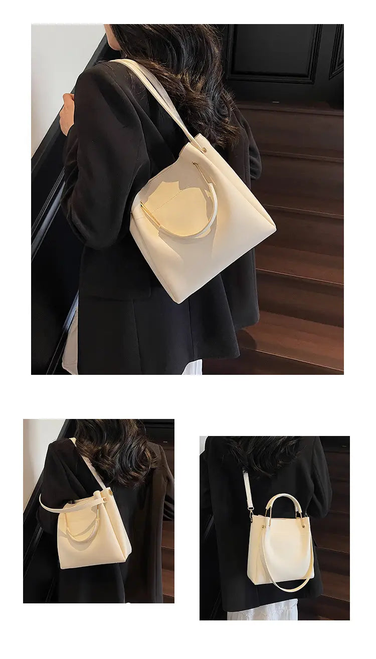 Cream-colored minimalist leather bucket bag with a rounded top handle and detachable adjustable shoulder strap.