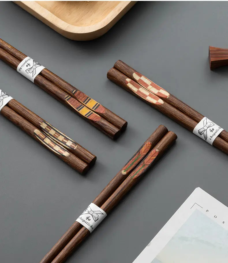 Dark brown wooden chopsticks with intricate checkered and leaf inlaid patterns secured by a white paper band with a bow illustration from a wooden chopsticks set with non slip tips 10 pairs.