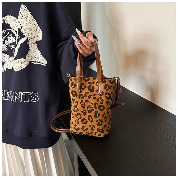 A tan and brown leopard print suede mini bucket crossbody bag with matching leather handles and a detachable shoulder strap.
