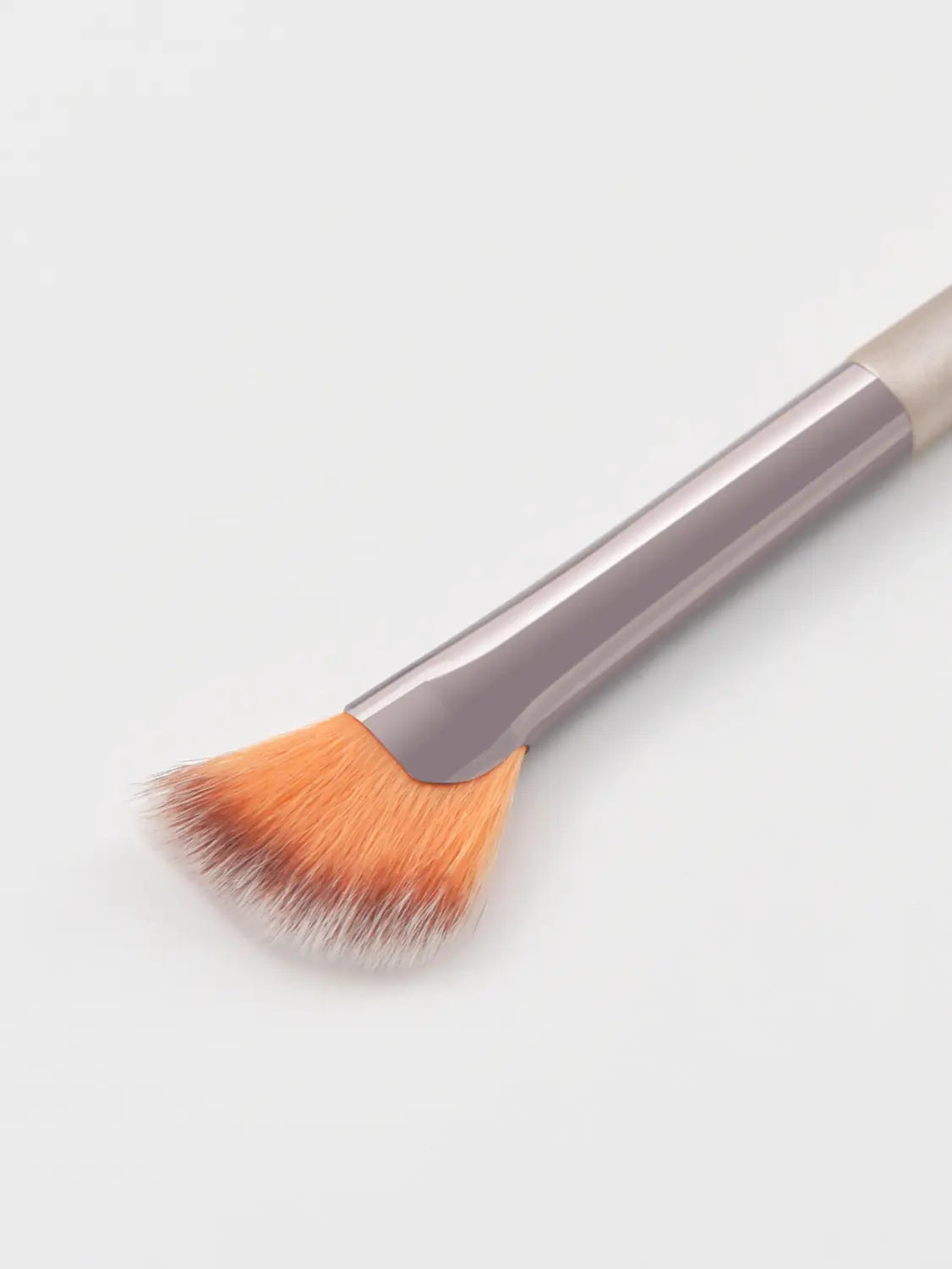 A sleek metallic-finish finger belly makeup brush with a tapered orange bristle head and gradient handle designed for professional contouring.