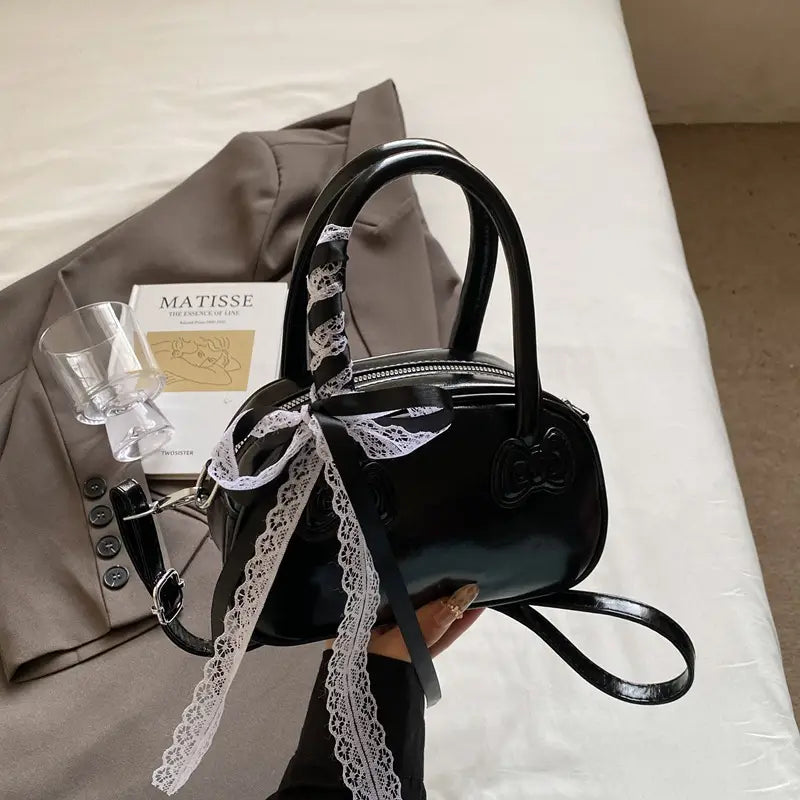 Hello Kitty glossy black handbag with white lace ribbon tied around the handle and a small bow detail on the front.