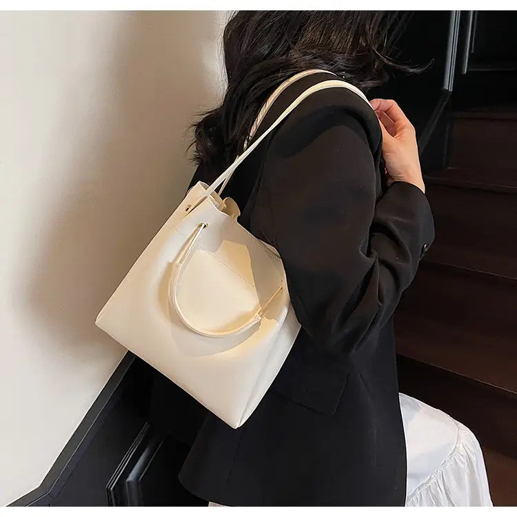 Cream-colored minimalist leather bucket bag with sleek design and matching top handle featuring a detachable strap.