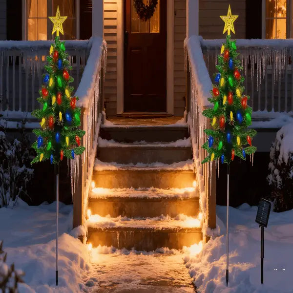 Two illuminated colorful LED solar Christmas tree lights with star toppers and icicle decorations for outdoor path decor.