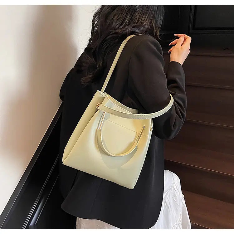 Cream-colored leather minimalist bucket bag with a top handle and detachable adjustable shoulder strap.