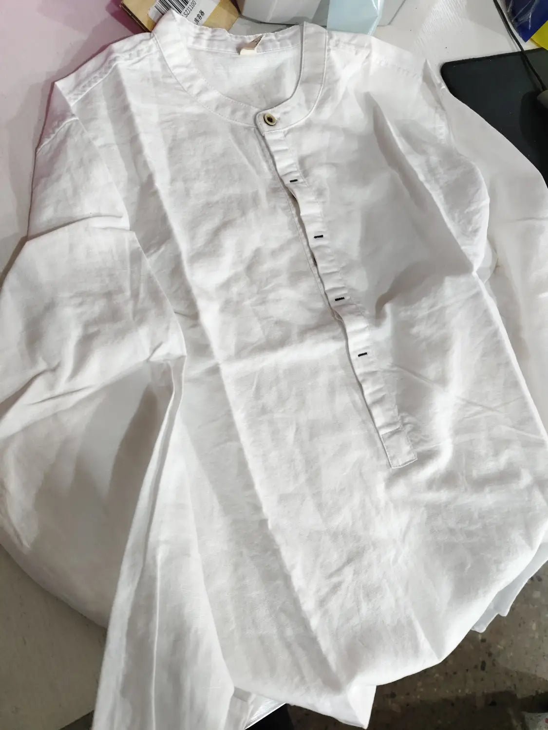 Men’s loose white linen long sleeve shirt with mandarin collar and black buttons.