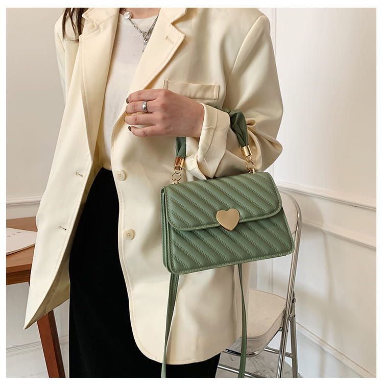 A mint green quilted crossbody bag with a gold heart-shaped clasp and matching shoulder strap featuring a ruched handle.