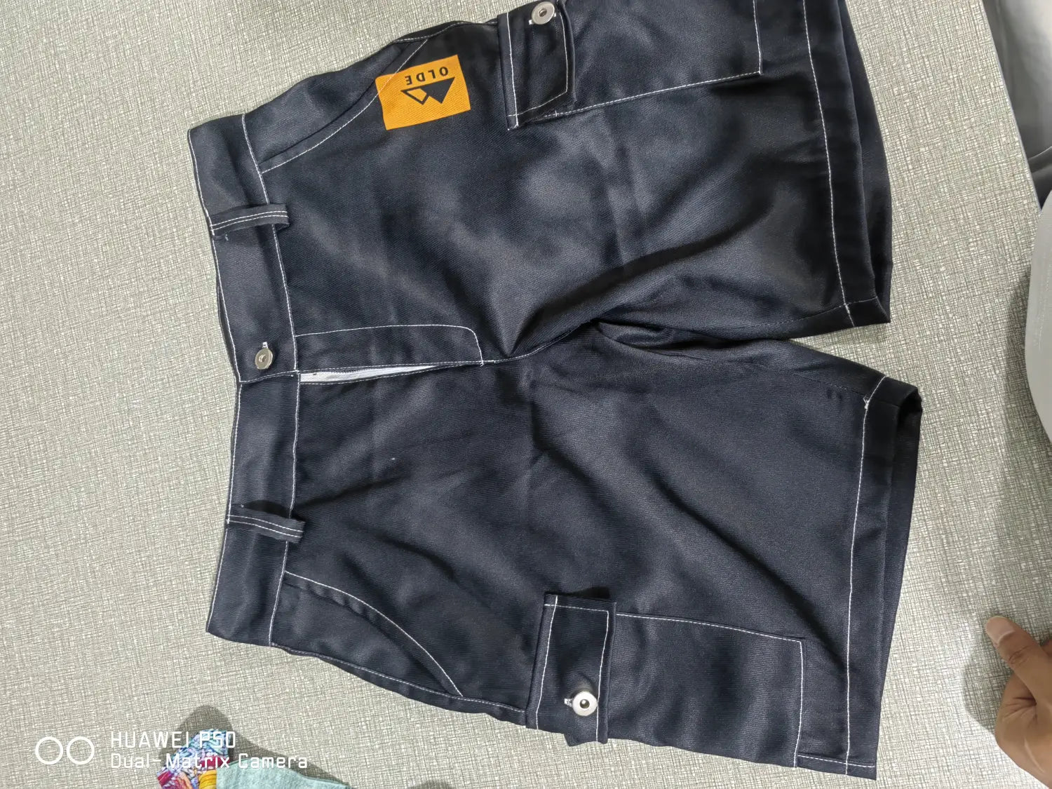the back side of dark blue polyester men’s digital print cargo shorts featuring white stitching and a yellow brand tag on the waistband.