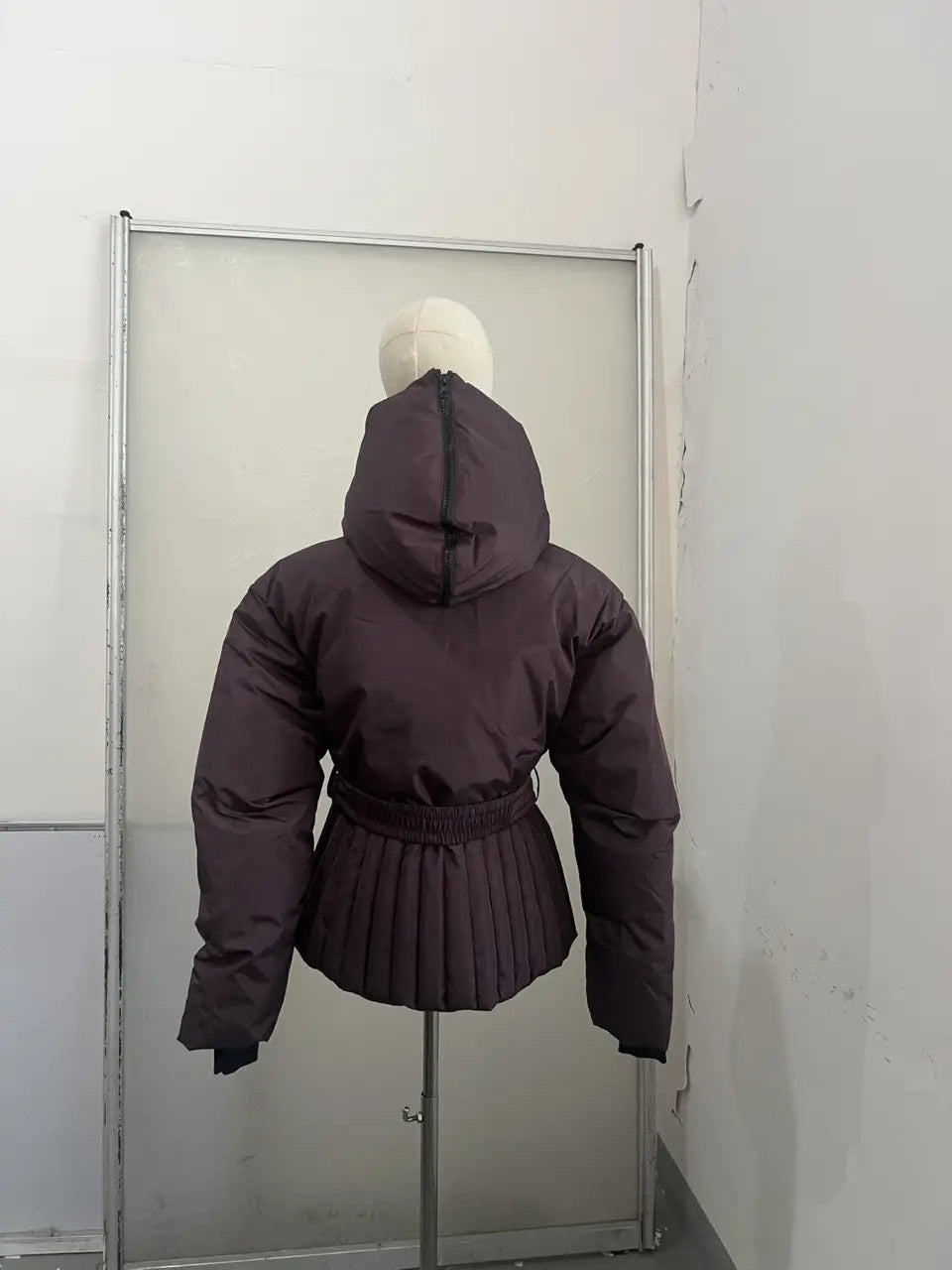 Women’s dark purple belted hooded puffer coat with elastic waistband and pleated skirt detail.