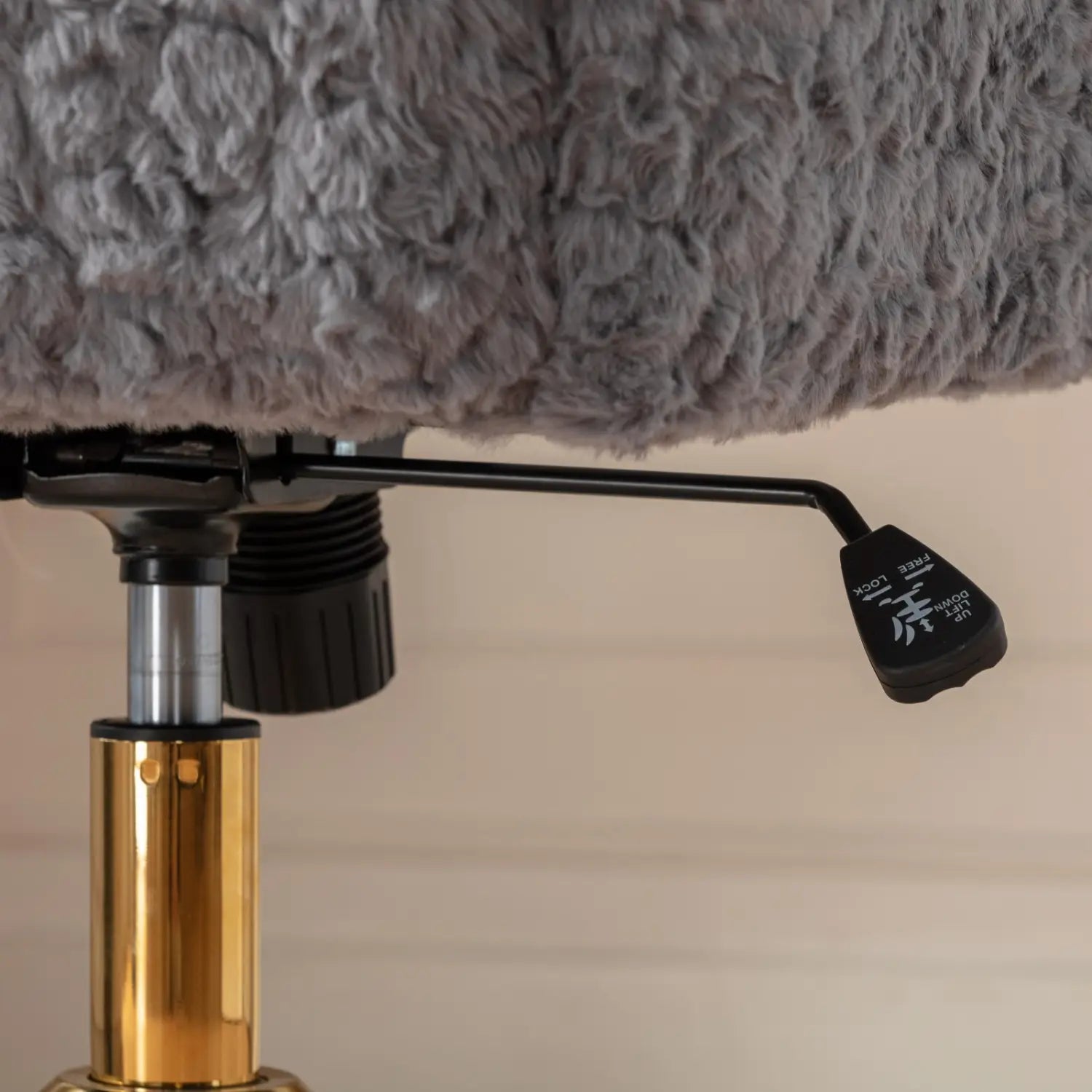 Chaise de bureau en fausse fourrure gris clair, avec une base en métal doré comportant un levier de réglage noir visible depuis l’arrière.
