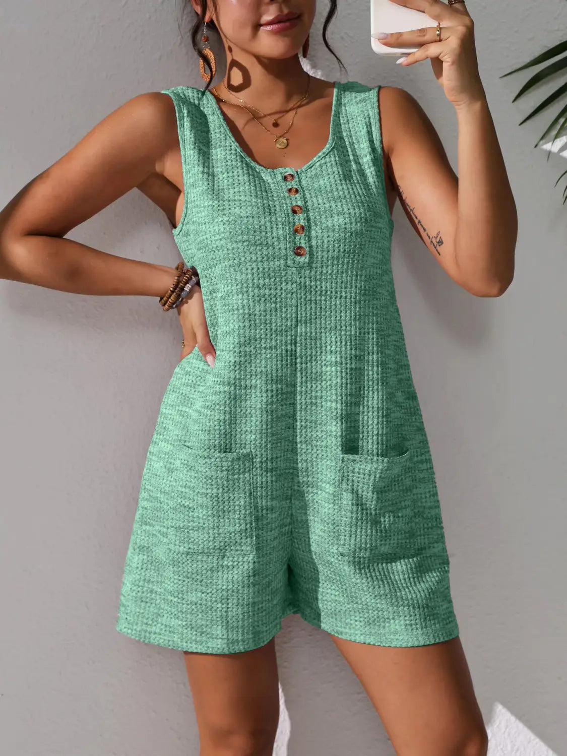 A mint green waffle knit sleeveless romper with a button-front neckline and two front pockets.