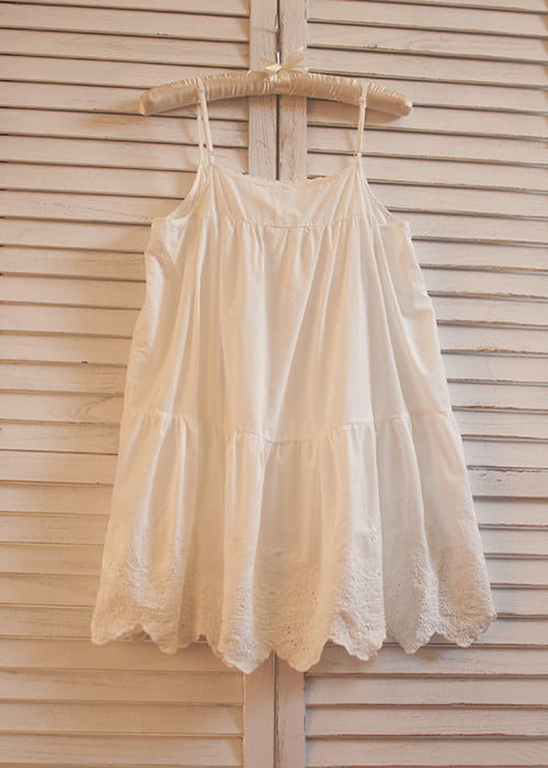 Ein zartes weißes Spitzenkleid mit Volants (gestufter Rock) mit Spitzenbesatz entlang des Saums, das an einem hölzernen Bügel hängt.