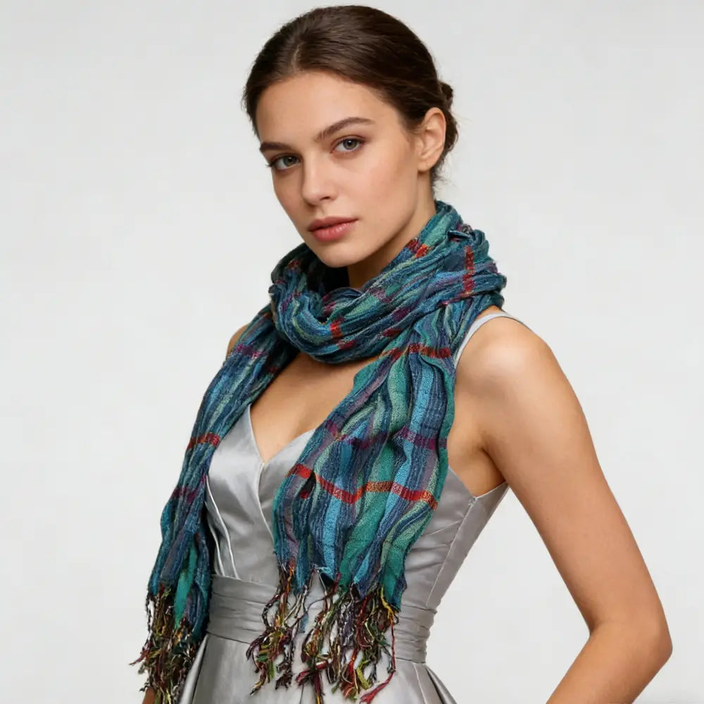 Une écharpe d’hiver bleu à jacquard texturé, présentant un motif écossais bleu et turquoise aux tons multiples, avec des accents rouges et des extrémités à franges.