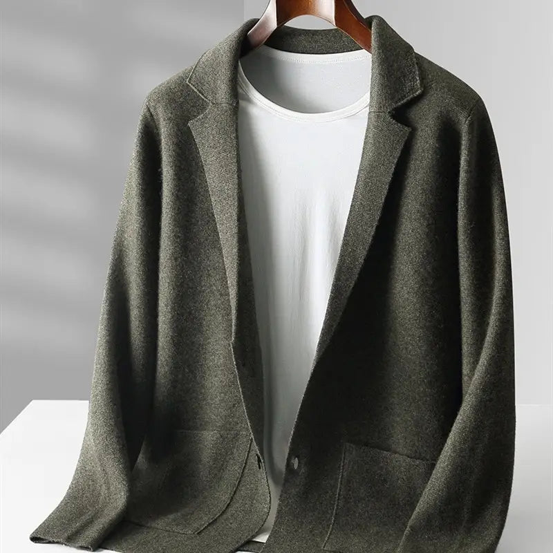 Herren V-Ausschnitt-Strickjacke aus olivgrünem Cardigan-Blazer aus dunkelolivgrünem Wollgemisch mit klassischem Revers und zwei vorderen aufgesetzten Taschen, dargestellt auf einem Holzaufhänger über einem weißen T-Shirt.