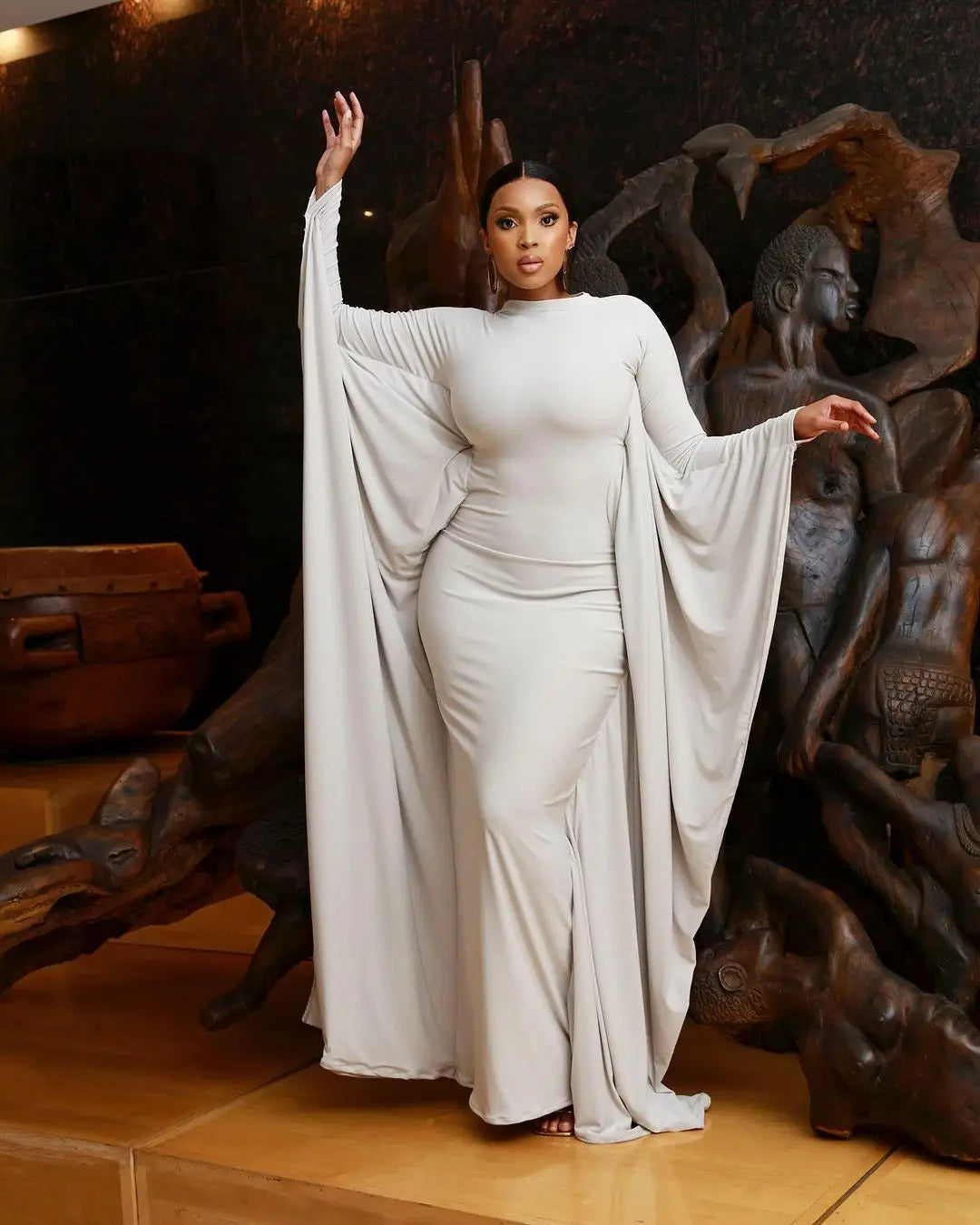 A sleek white asymmetrical satin maxi dress with batwing sleeves and a high neckline.