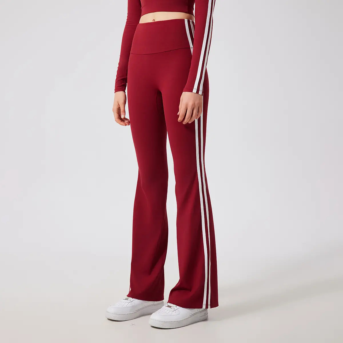 Leggings de yoga évasés taille haute bordeaux fabriqués dans un tissu de type survêtement, avec des bandes latérales blanches.