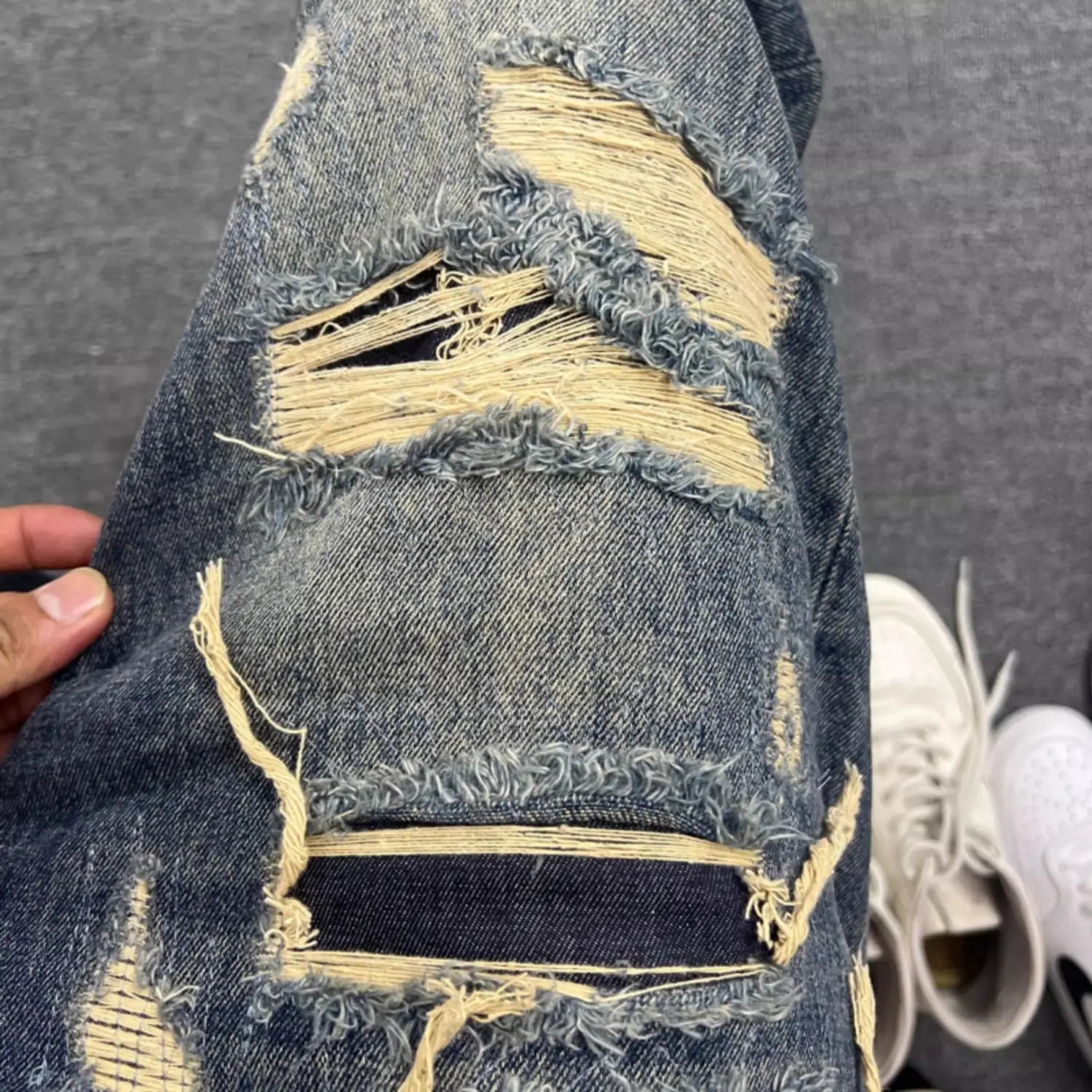 Men’s light blue distressed ripped patch denim jeans featuring frayed holes and exposed yellowish stitching.