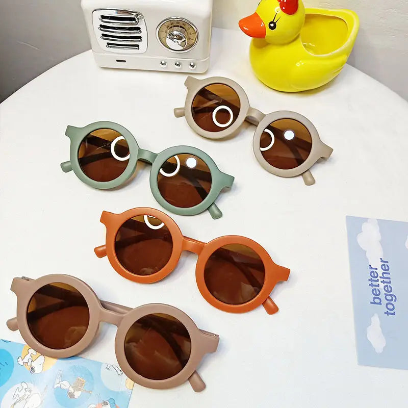 Lot de quatre lunettes de soleil pour enfants rondes avec des montures vert pastel, orange et beige, et des verres marron, présentant un motif rétro de chien en forme de cercle avec une monture orange.