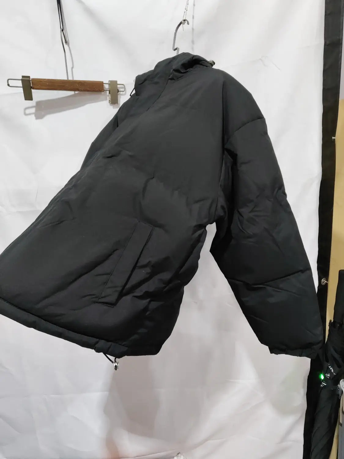 Beige Damen-Kapuzensteppjacke mit wattierter Polsterung in Schwarz mit Stepp-Design, die an einem hölzernen Kleiderbügel hängt