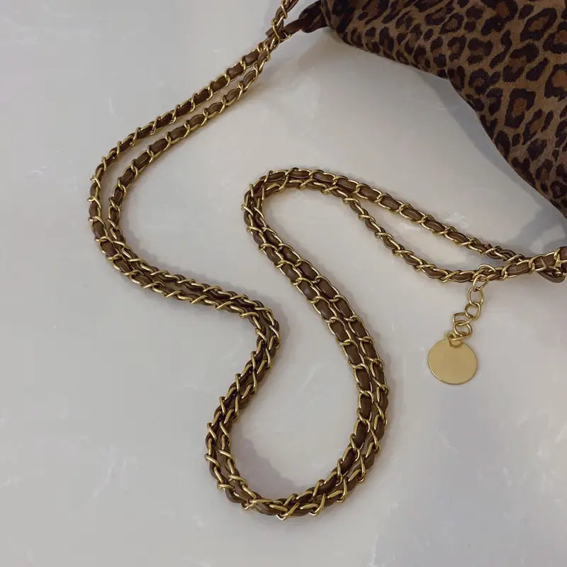 Leopard print crossbody bag with a gold-toned chain strap featuring a classic interlocking link design and a small circular tag at the end.