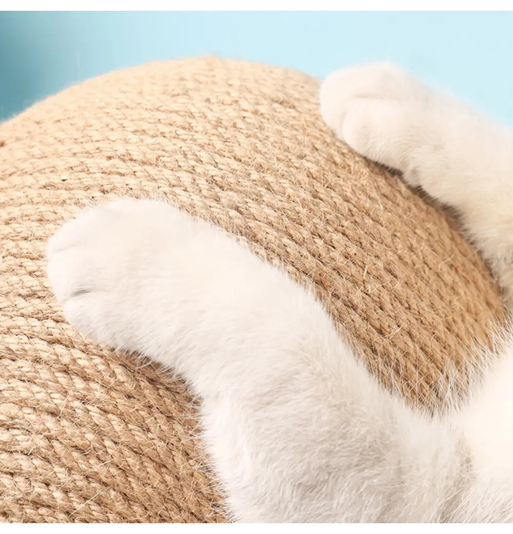 Una pelota de rascado redonda de cuerda de sisal beige para gato, con una superficie con textura y patas de felpa blanca y suave, apoyada en ella, mostrada con un soporte triangular de madera.