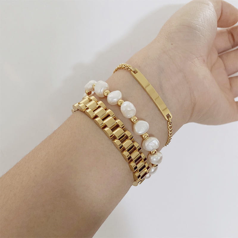 Elegant gold titanium watch-style bracelet featuring a sleek interlocking link design with pearl accents.