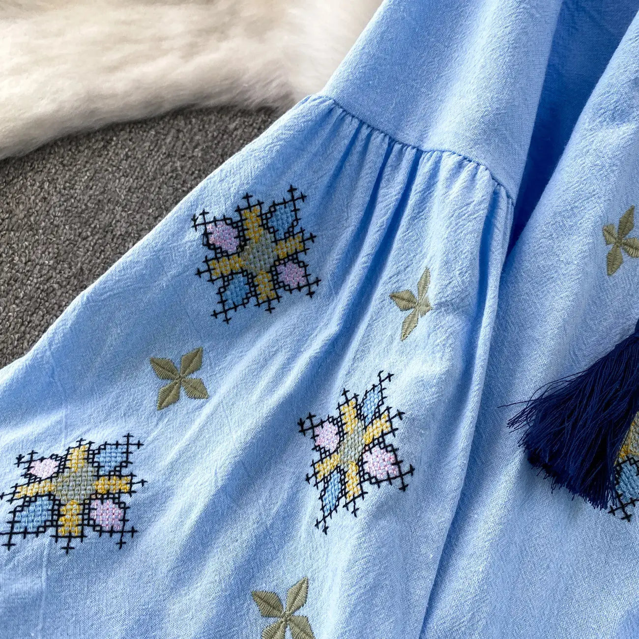 Embroidered lantern sleeve tie neck blouse in light blue with intricate cross-stitch floral patterns in yellow pink and green.