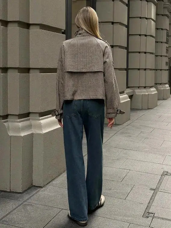A woman wearing a beige and black houndstooth patterned cropped coat with belted cuffs in a relaxed fit double breasted jacket.