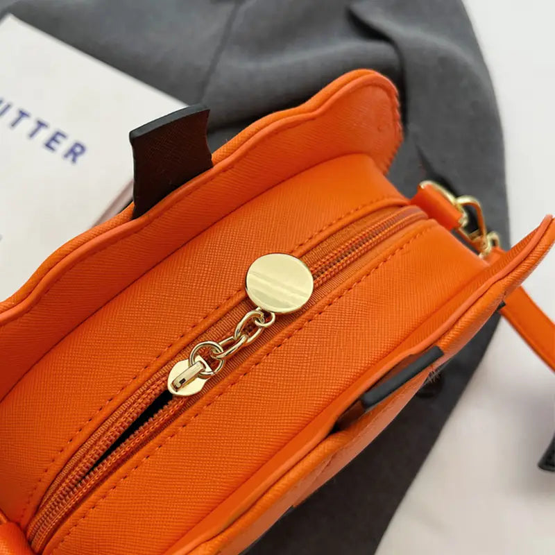 Bright orange faux leather crossbody bag with gold-tone zipper pull and chain detail featuring a funny pumpkin and bat design with detachable charm.