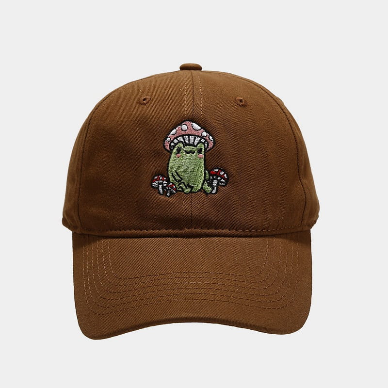 Brown cotton baseball cap featuring a colorful embroidered design of a green frog sitting under a pink and white mushroom with smaller mushrooms around it.