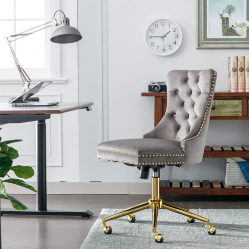 Chaise de bureau en velours capitonné gris avec piètement pivotant en métal à finition ton sur ton or et garniture à clous décoratifs, conçue pour une utilisation au bureau.