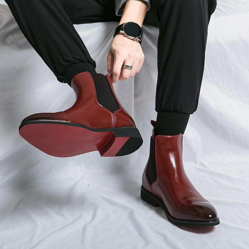 Men’s black patent leather Chelsea boots feature a shiny burgundy leather upper with black rubber soles and elastic side panels.