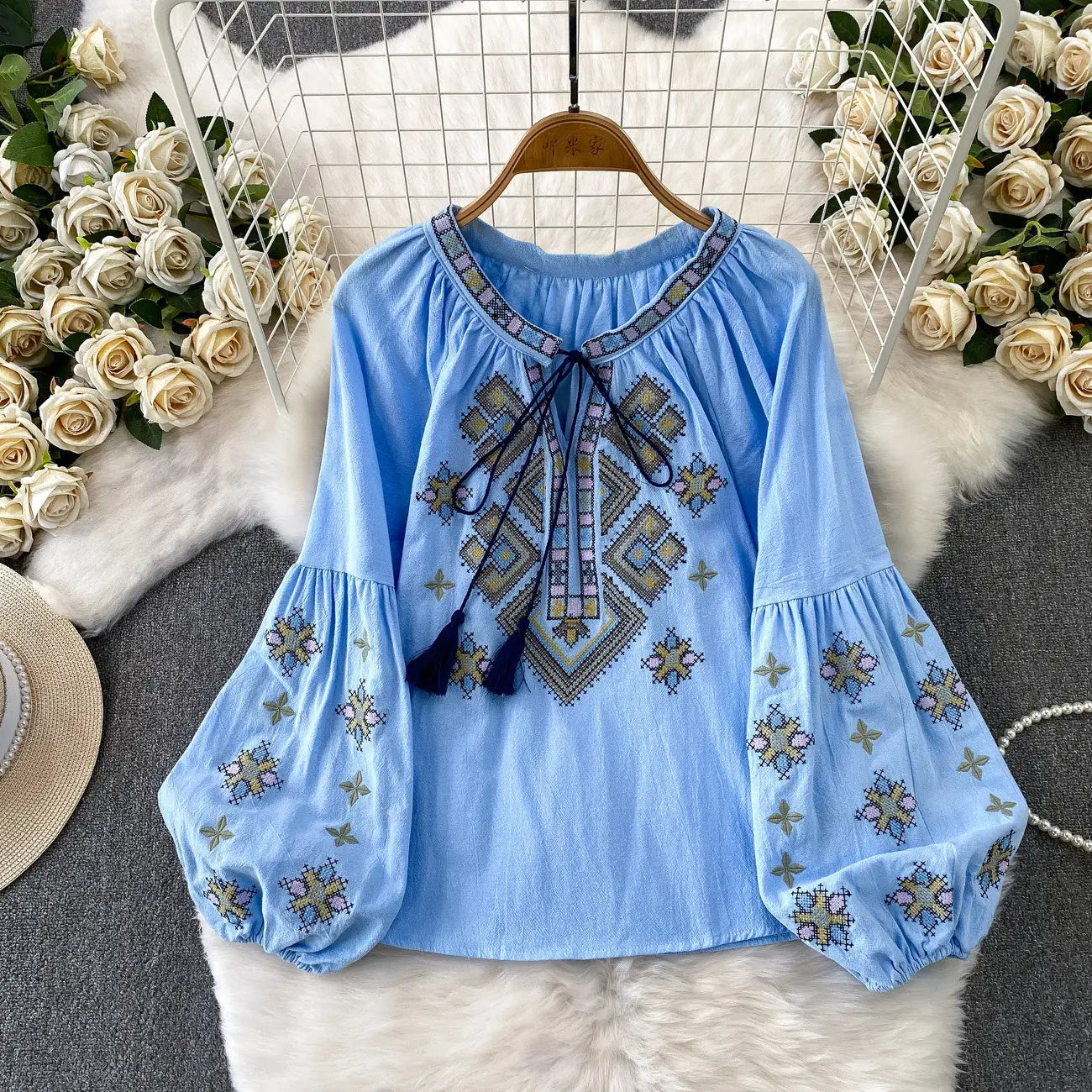 Light blue embroidered lantern sleeve tie neck blouse with long puffed sleeves and geometric gold beige and navy thread pattern.