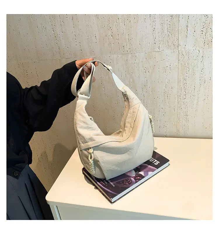 Beige canvas nylon crossbody bag with large capacity hobo design featuring an adjustable shoulder strap and decorative braided cord accents.