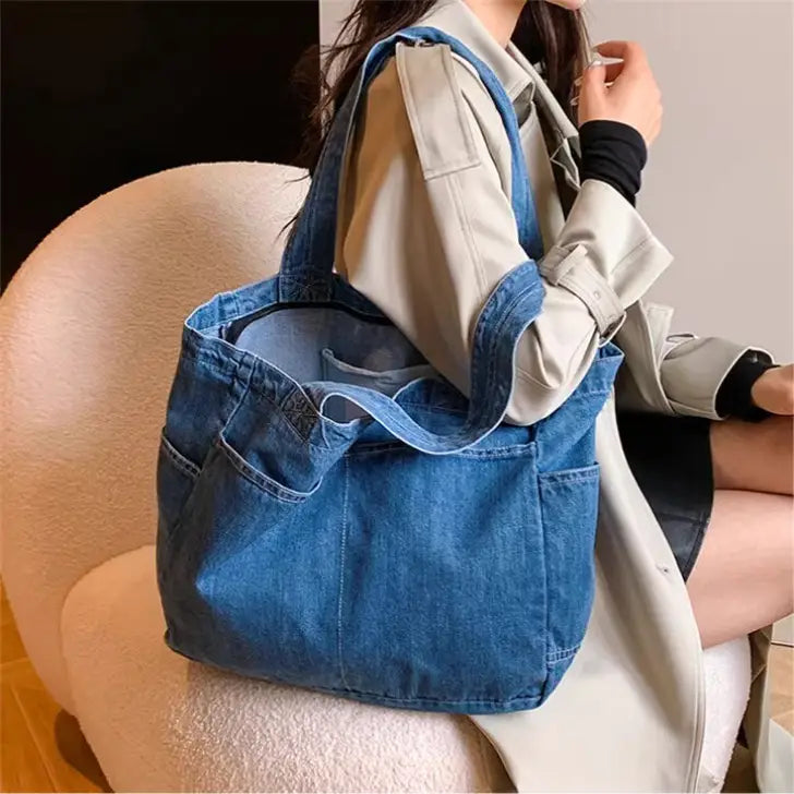Blue denim tote bag with large capacity, multiple pockets, and sturdy handles, designed for shoulder use by Alma Latina.