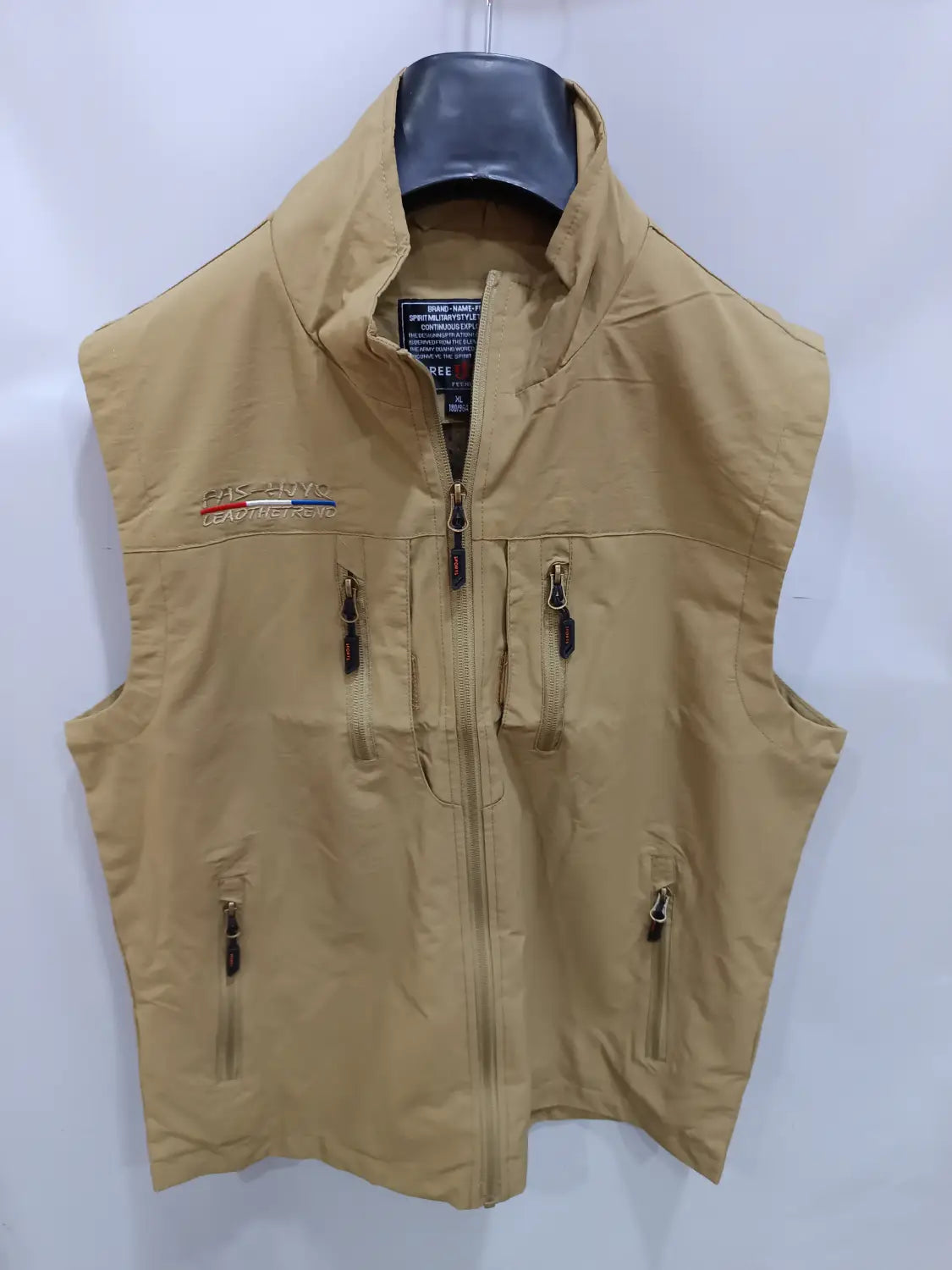 Chaleco utilitario con capucha impermeable color arena para hombre con varios bolsillos con cremallera y logotipo de la marca bordado en el lado izquierdo del pecho.