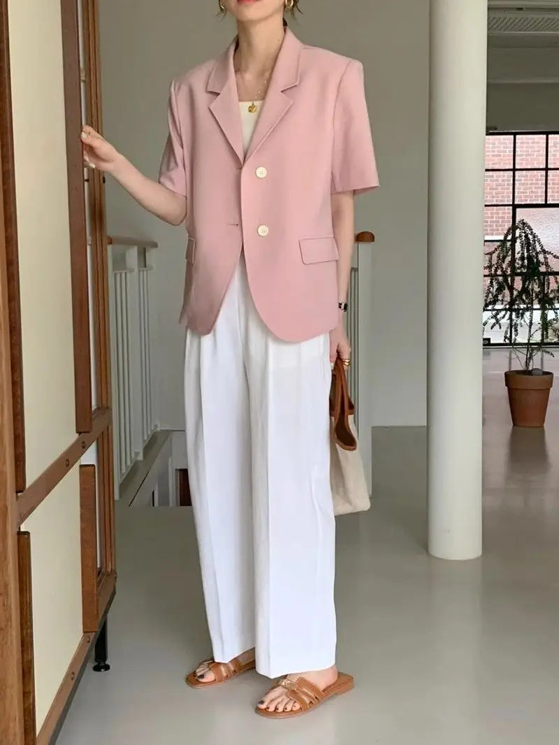 Un blazer pour femmes rose pâle à manches courtes, avec une coupe structurée et deux boutons à l’avant, conçu comme une veste décontractée à coupe décontractée.
