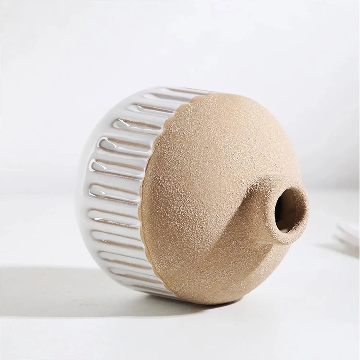 A two toned ceramic flower vase with a matte beige body and a glossy white ribbed neck featuring a small opening ideal for boho tabletop decor.