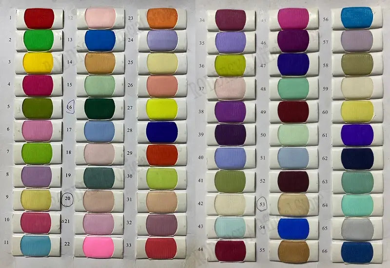 Une robe de mariée sur mesure en style sirène présentant un design bustier en dentelle est complétée par un assortiment éclatant d’échantillons de tissu en satin, dans des couleurs et des nuances variées, disposés avec soin sur un fond blanc